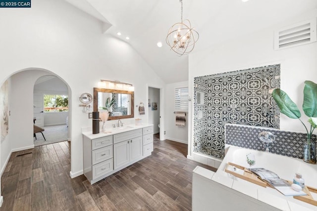 bathroom with an inviting chandelier, a washtub, vanity, and high vaulted ceiling