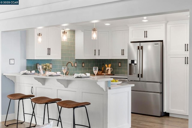 kitchen featuring high end refrigerator, light hardwood / wood-style floors, a kitchen bar, hanging light fixtures, and white cabinets