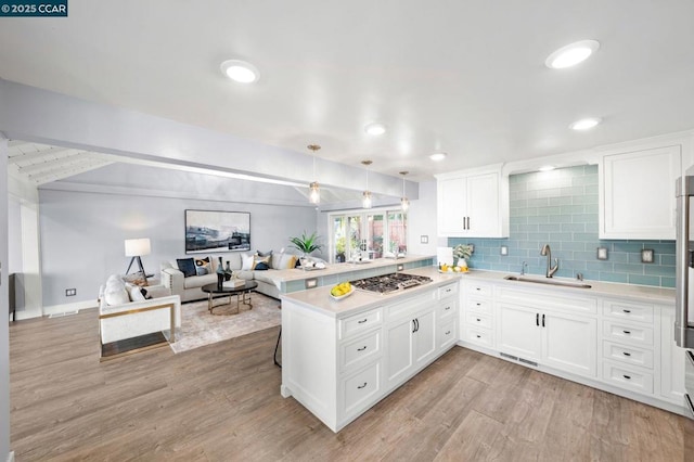 kitchen with hanging light fixtures, kitchen peninsula, stainless steel gas stovetop, and white cabinetry