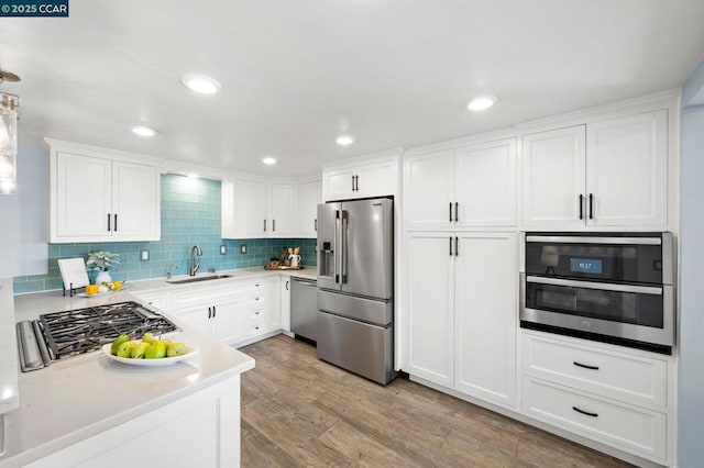 kitchen with appliances with stainless steel finishes, sink, white cabinetry, and light hardwood / wood-style flooring