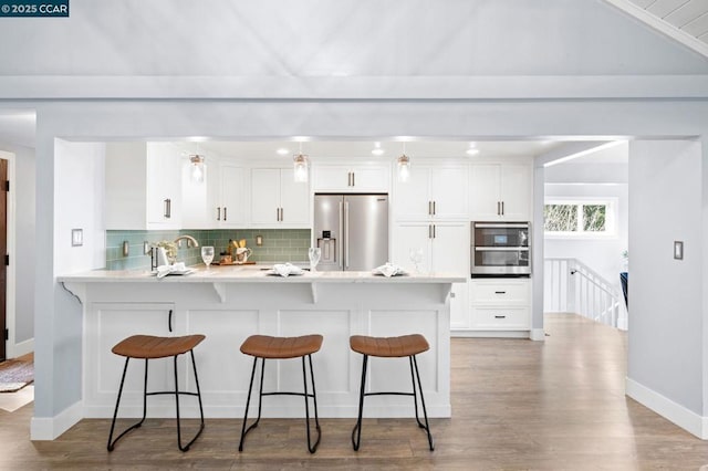 kitchen with kitchen peninsula, white cabinets, stainless steel appliances, and tasteful backsplash