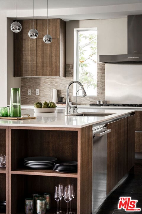 kitchen with backsplash, wall chimney range hood, pendant lighting, sink, and dark brown cabinets