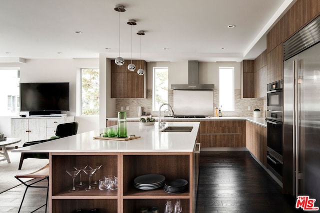 kitchen featuring an island with sink, sink, wall chimney range hood, and stainless steel appliances