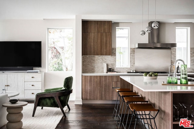 kitchen with pendant lighting, plenty of natural light, a breakfast bar, and wall chimney range hood