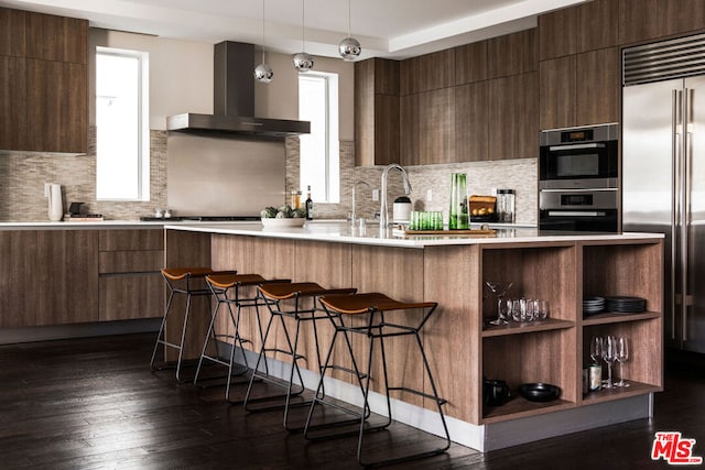 kitchen featuring stainless steel appliances, a healthy amount of sunlight, dark hardwood / wood-style flooring, hanging light fixtures, and wall chimney exhaust hood