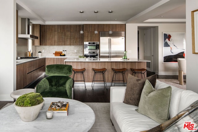 kitchen featuring pendant lighting, appliances with stainless steel finishes, a center island, wall chimney range hood, and a breakfast bar area