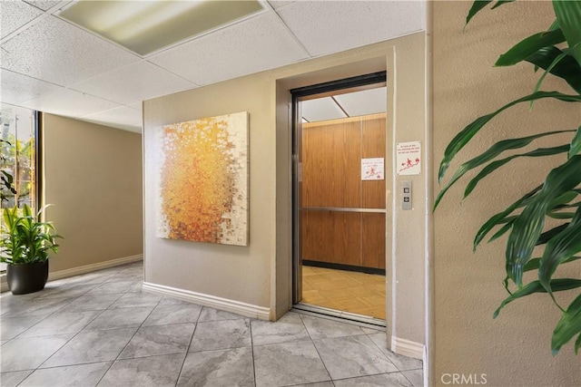 corridor featuring light tile patterned floors, a drop ceiling, and elevator