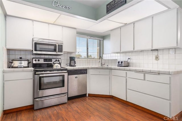 kitchen with dark hardwood / wood-style floors, appliances with stainless steel finishes, white cabinets, and tile counters