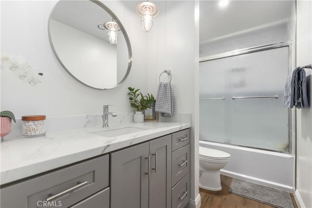 full bathroom with toilet, enclosed tub / shower combo, hardwood / wood-style floors, and vanity