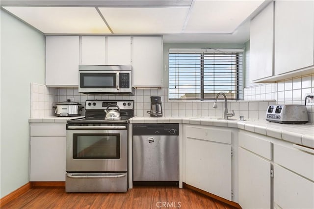 kitchen with appliances with stainless steel finishes, sink, white cabinetry, and hardwood / wood-style flooring