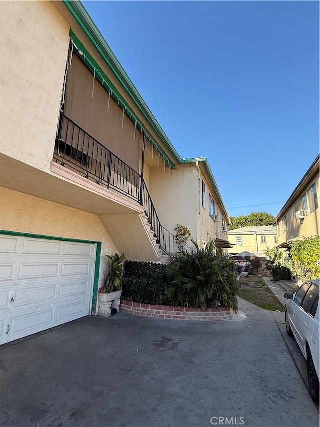 view of side of property with driveway, stairway, an attached garage, and stucco siding