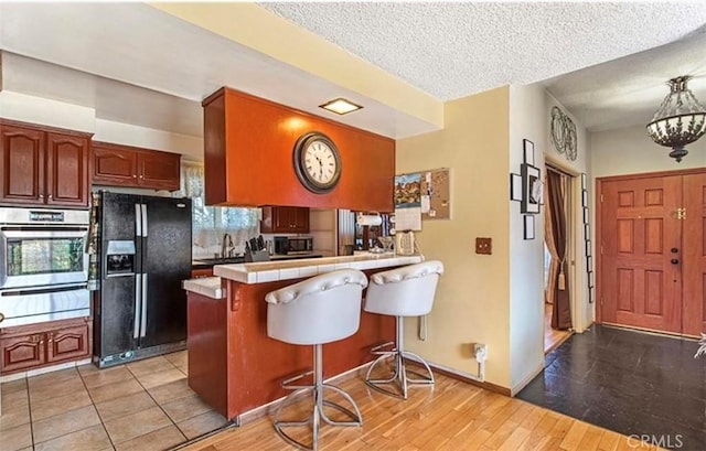 kitchen featuring kitchen peninsula, appliances with stainless steel finishes, a breakfast bar area, a textured ceiling, and tile counters