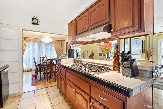 kitchen featuring dishwasher, stainless steel gas stovetop, tile countertops, a notable chandelier, and light tile patterned floors