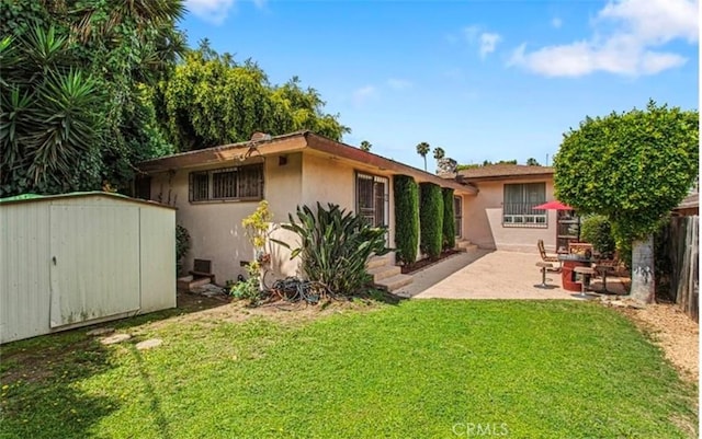 rear view of property featuring a lawn, a storage unit, and a patio area