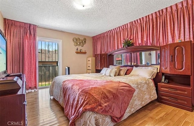 bedroom featuring light wood-type flooring, access to exterior, and a textured ceiling