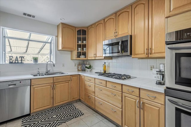 kitchen featuring decorative backsplash, sink, appliances with stainless steel finishes, tile counters, and light tile patterned floors