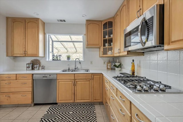 kitchen featuring light tile patterned floors, tile countertops, appliances with stainless steel finishes, backsplash, and sink