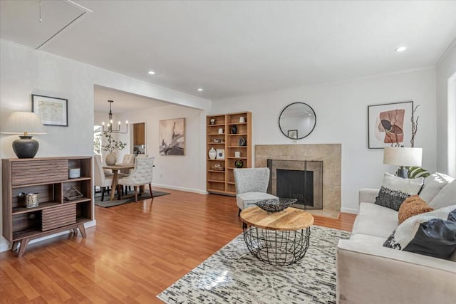 living room featuring light wood-type flooring, a notable chandelier, and a tiled fireplace