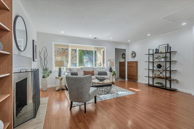 living room featuring a tile fireplace, ornamental molding, and light wood-type flooring