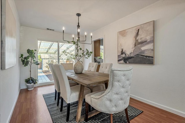 dining area with dark hardwood / wood-style floors, ornamental molding, and an inviting chandelier