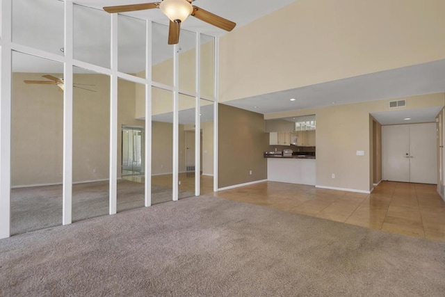 unfurnished living room featuring ceiling fan, light tile patterned floors, and a towering ceiling