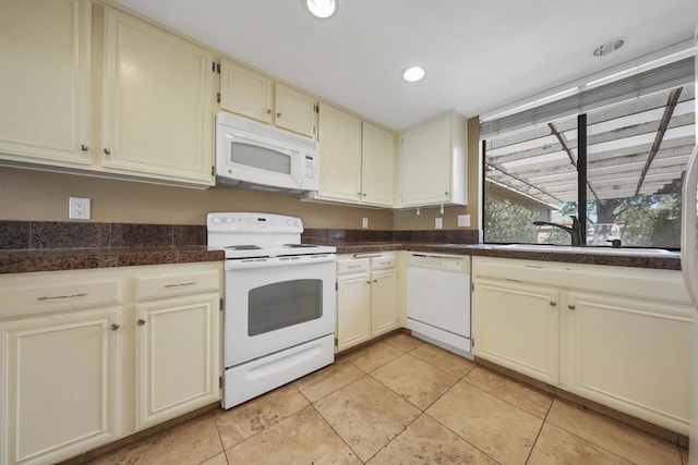 kitchen with sink, white appliances, light tile patterned floors, and cream cabinetry