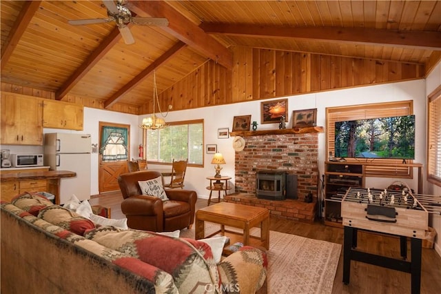 living room with wood ceiling, ceiling fan with notable chandelier, a wood stove, wood-type flooring, and beam ceiling