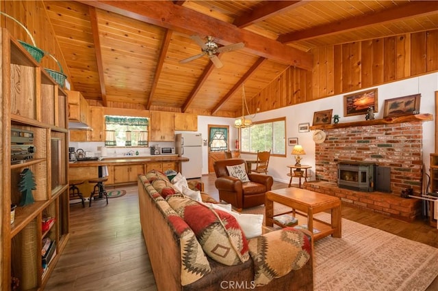 living room featuring a wealth of natural light, dark wood-type flooring, beamed ceiling, and a wood stove