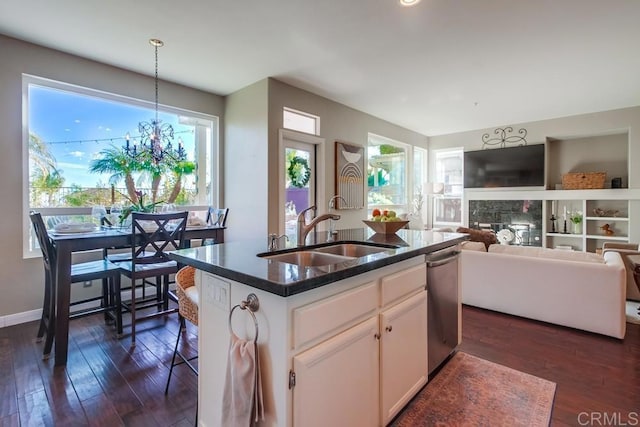 kitchen with a sink, white cabinetry, hanging light fixtures, an island with sink, and dark countertops