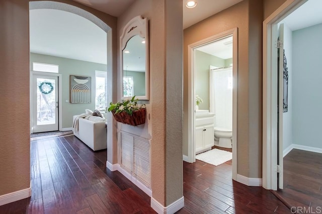 hallway featuring dark wood-style floors, recessed lighting, arched walkways, and baseboards