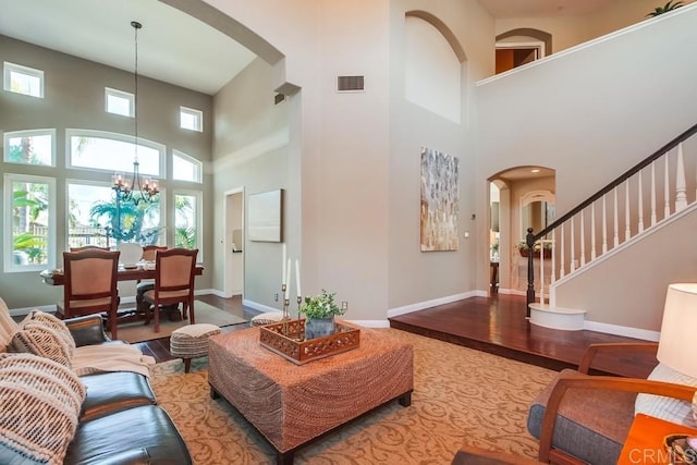 living area featuring arched walkways, a chandelier, wood finished floors, visible vents, and baseboards