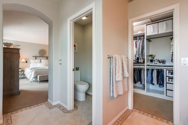 bathroom featuring a walk in closet, baseboards, toilet, and tile patterned floors