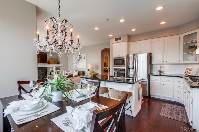 dining area with arched walkways, a fireplace, recessed lighting, visible vents, and dark wood-type flooring