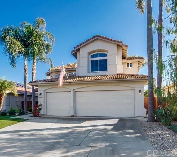 mediterranean / spanish-style house with a garage, driveway, a tiled roof, and stucco siding