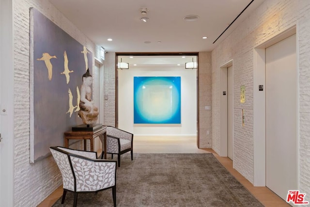 hallway with elevator, brick wall, and light hardwood / wood-style floors