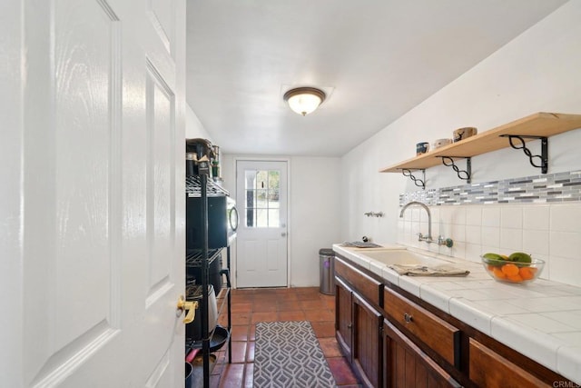 kitchen with tile countertops, decorative backsplash, sink, dark tile patterned floors, and dark brown cabinets