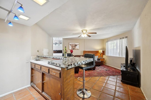 kitchen with kitchen peninsula, ceiling fan, tile counters, a kitchen breakfast bar, and tile patterned floors