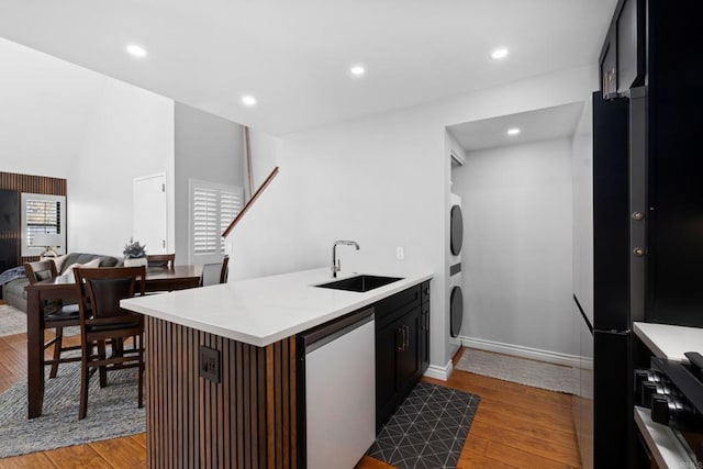 kitchen featuring stacked washer / drying machine, sink, kitchen peninsula, stainless steel dishwasher, and light hardwood / wood-style flooring