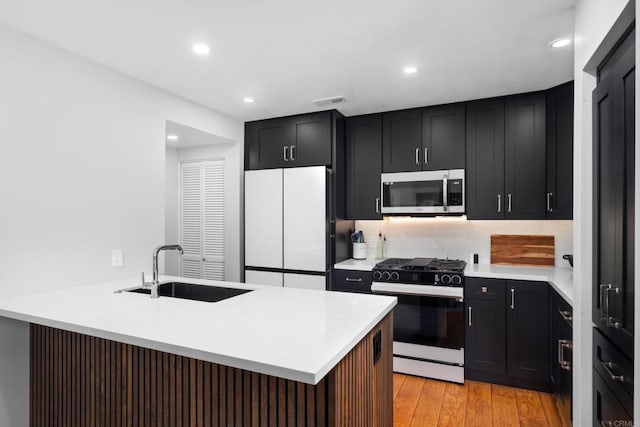 kitchen featuring range with gas stovetop, white fridge, sink, light hardwood / wood-style flooring, and a breakfast bar area