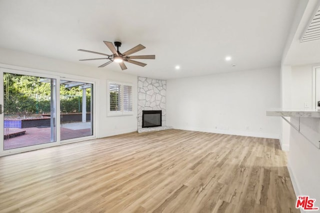 unfurnished living room with ceiling fan, light hardwood / wood-style floors, and a stone fireplace