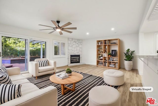 living room with ceiling fan, a stone fireplace, and light hardwood / wood-style flooring