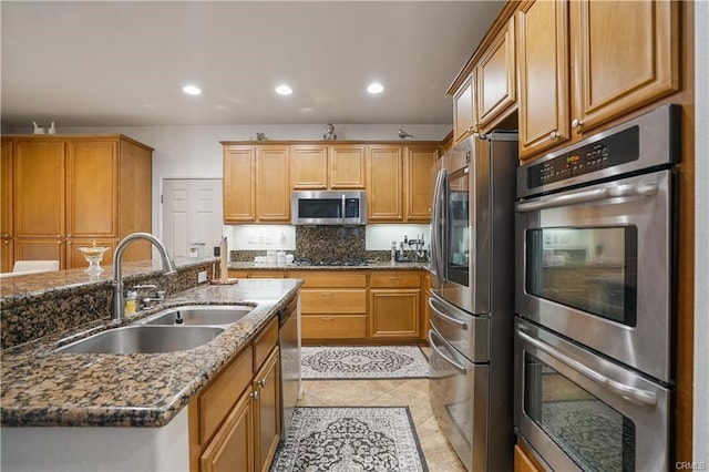 kitchen with a center island with sink, appliances with stainless steel finishes, tasteful backsplash, dark stone counters, and sink