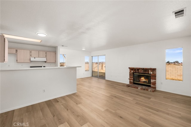 unfurnished living room with a brick fireplace, a textured ceiling, and light hardwood / wood-style flooring