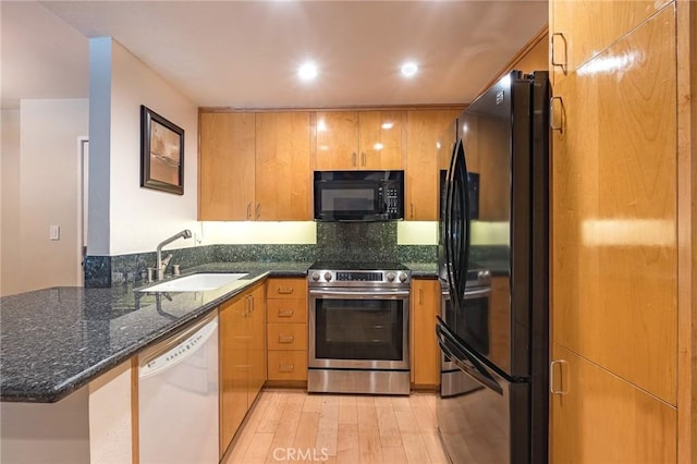 kitchen with black appliances, kitchen peninsula, sink, light wood-type flooring, and dark stone counters