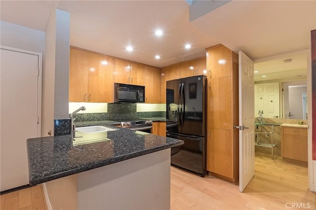 kitchen featuring light hardwood / wood-style floors, kitchen peninsula, dark stone counters, black appliances, and sink