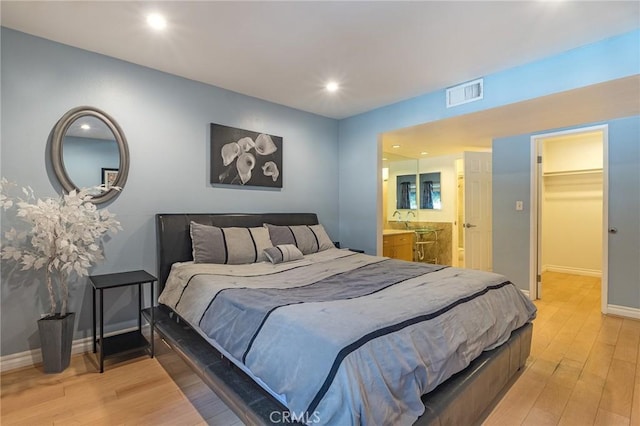 bedroom featuring a walk in closet, connected bathroom, sink, a closet, and light wood-type flooring