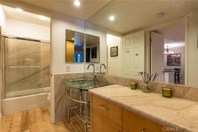 full bathroom with toilet, a notable chandelier, bath / shower combo with glass door, wood-type flooring, and vanity