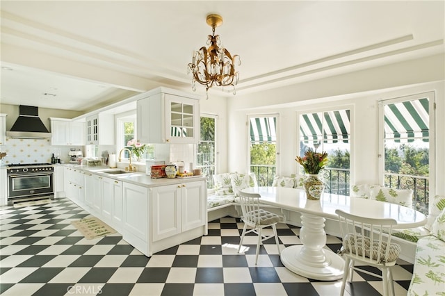 kitchen featuring high end range, wall chimney range hood, white cabinetry, and tasteful backsplash