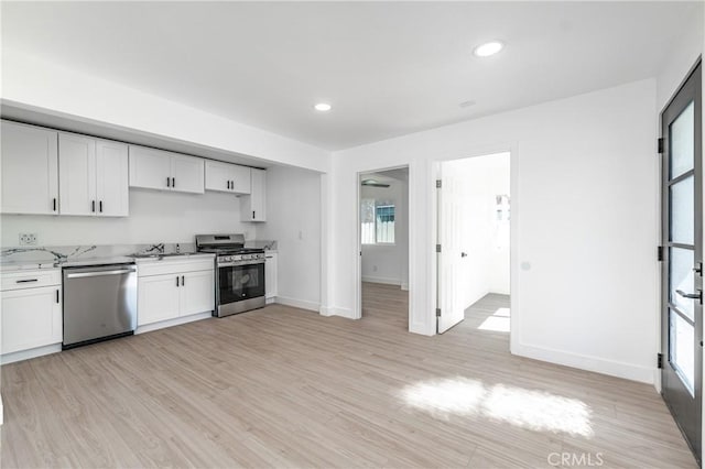 kitchen featuring white cabinetry, appliances with stainless steel finishes, light hardwood / wood-style flooring, light stone counters, and sink