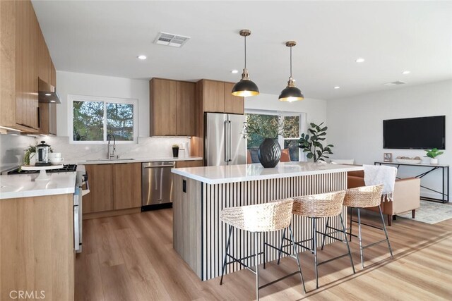 kitchen with a center island, decorative light fixtures, stainless steel appliances, sink, and ventilation hood